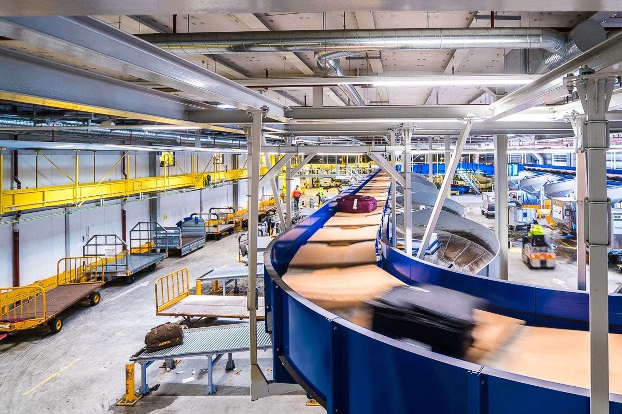 Conveyor belt for suitcases, seen from inside the staff area - large trolleys and staff driving around on airport trolleys