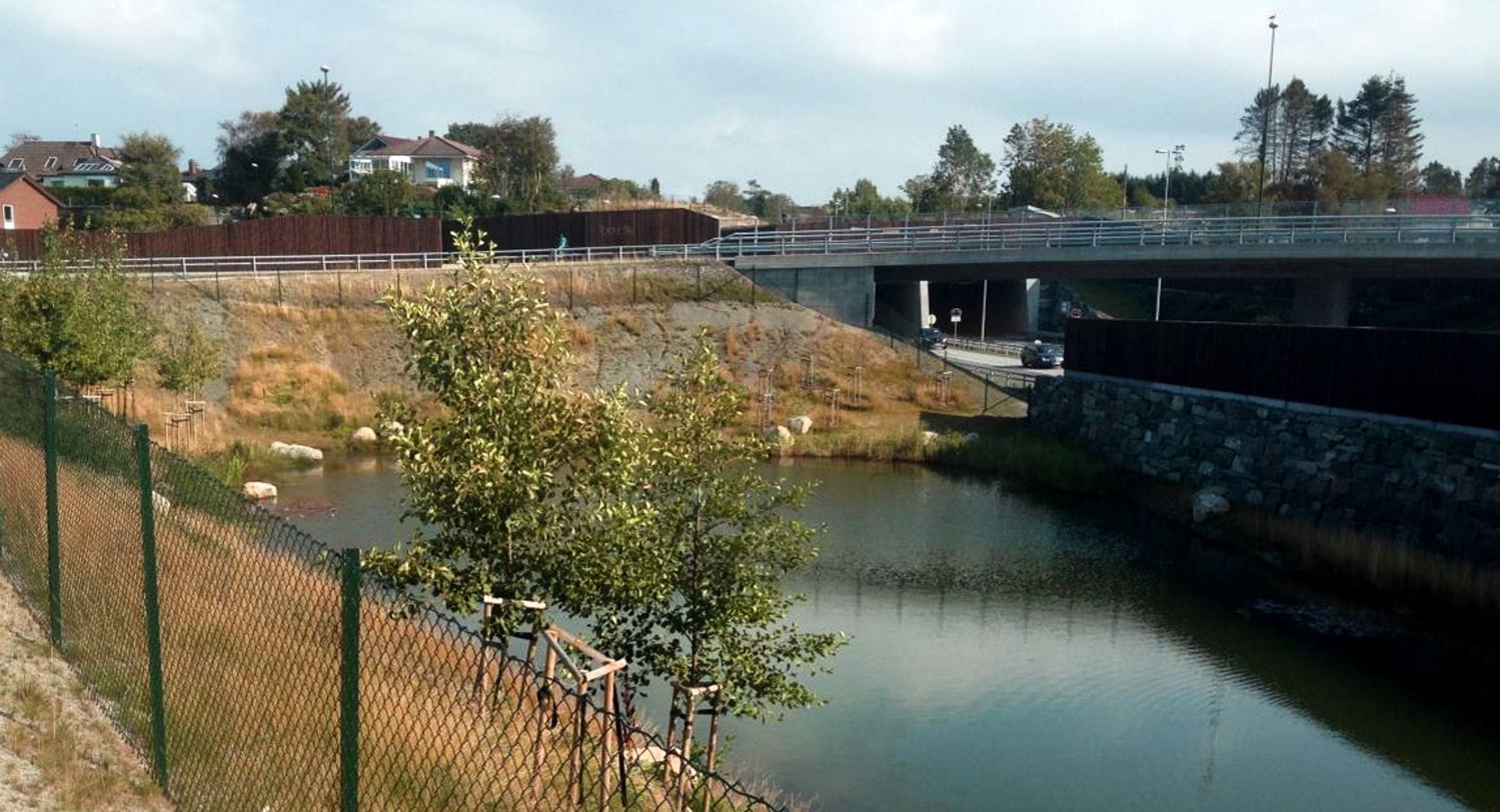 riverbed with railings on the right, a bridge spanning the water, trees and buildings in the distance