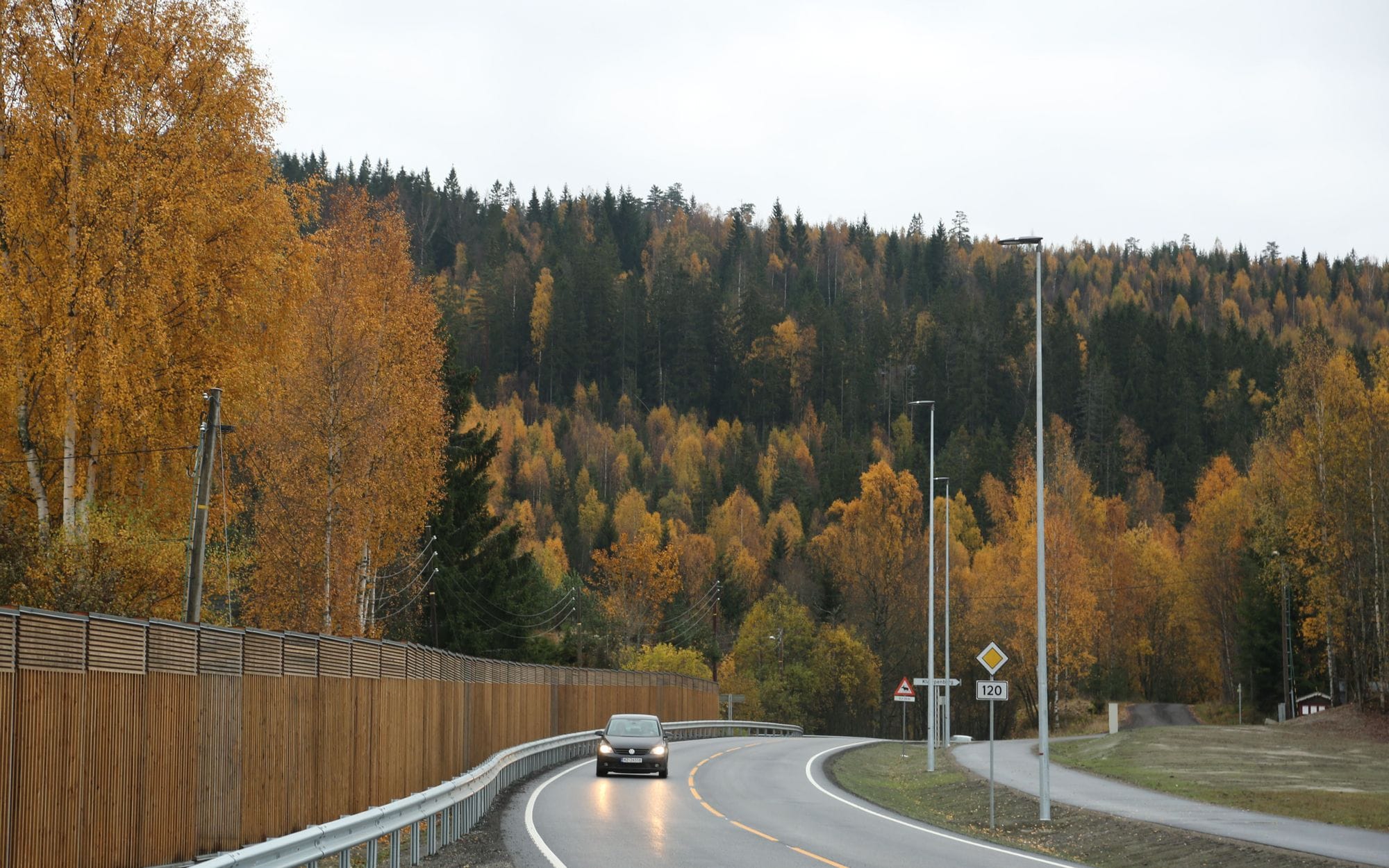 A car driving on a road surrounded by tree and traffic lights in Norway